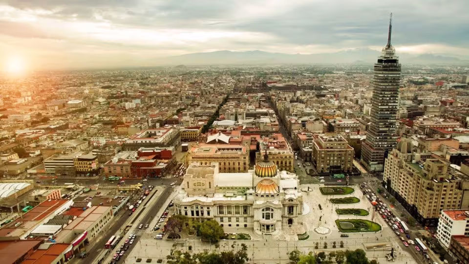 Aerial view of Mexico City featuring the Palace of Fine Arts and the Torre Latinoamericana under a bright sky.