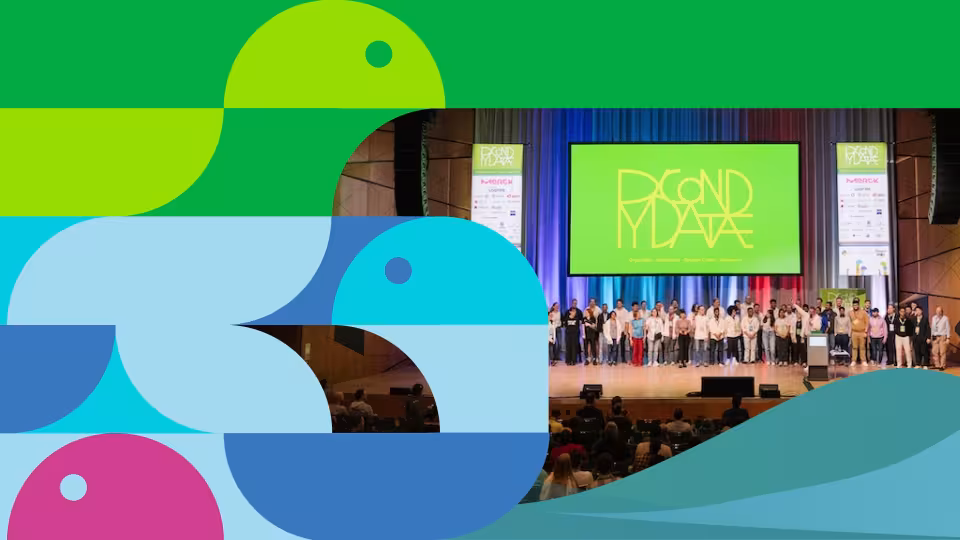 Abstract geometric bird-like shapes in green, blue, pink, and light blue overlap on the left, while the right side shows an auditorium stage where a large group of people stand facing an audience. A large screen behind them reads "BECOND YEAR" in yellow letters, and two smaller screens display "Merck". In the foreground, an audience sits in an auditorium. Teal waves are across the bottom right.