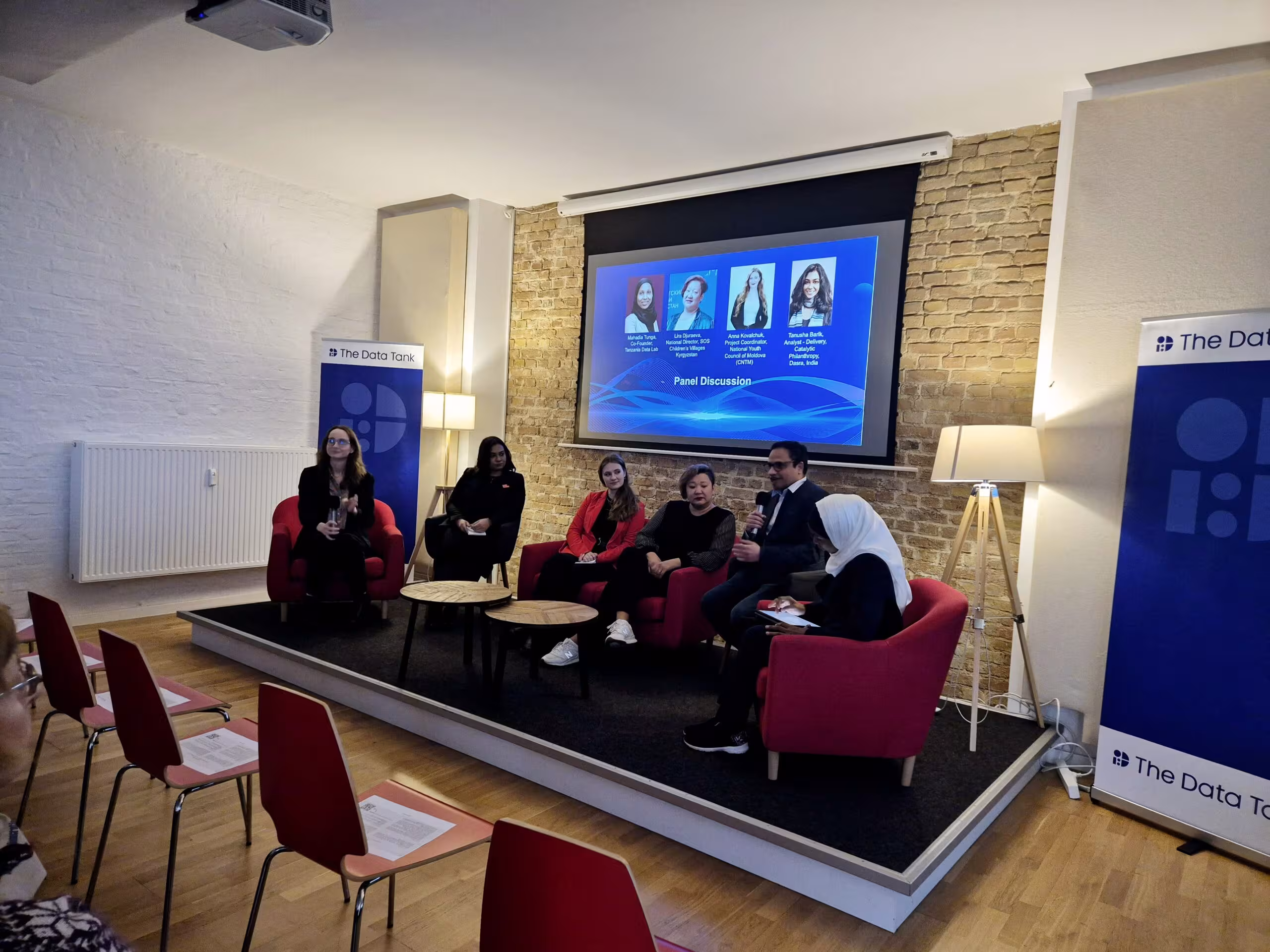 panel of speakers sitting in front of silver screen with presentation
